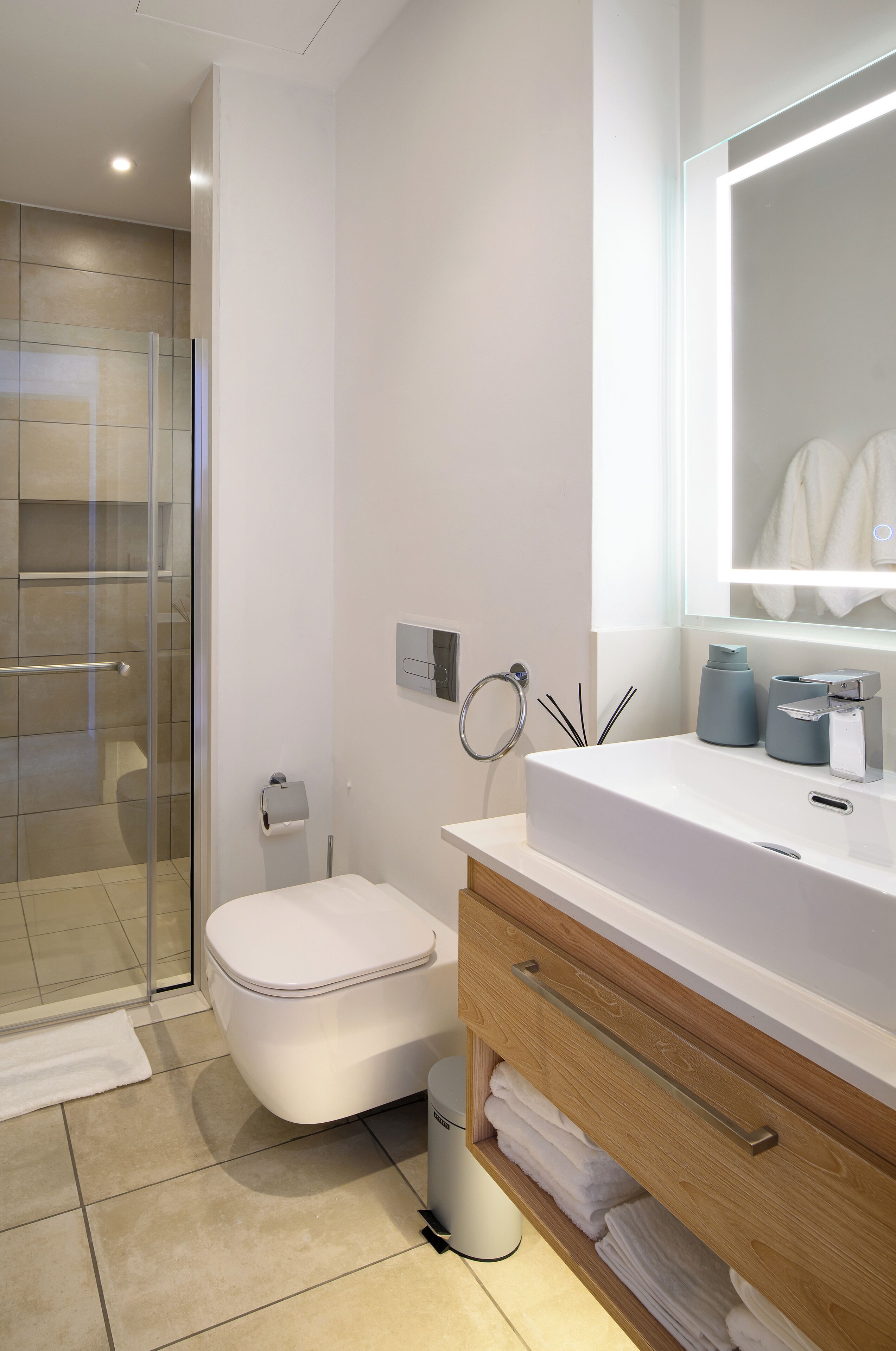 A modern bathroom with a glass shower enclosure, a white toilet, a vanity with a mirror, and a towel rack.