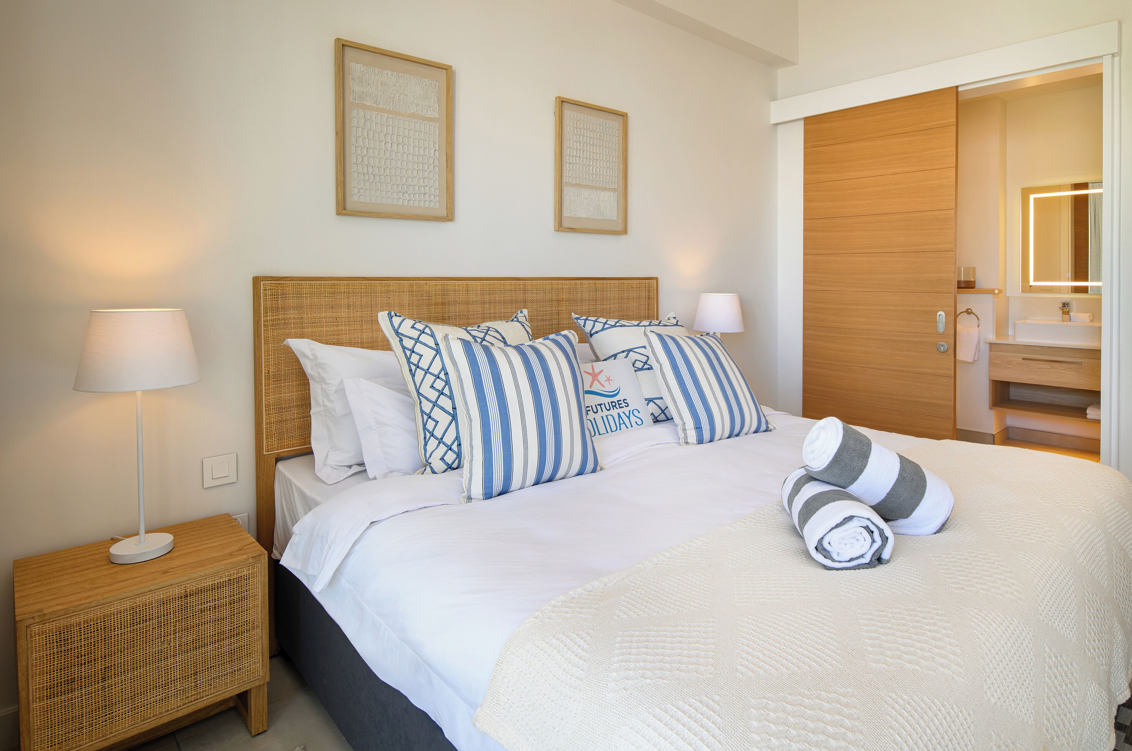 A neatly made bed with striped pillows, a bedside lamp, and a rolled towel on the bed.