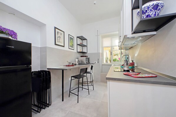 A modern kitchen with a black refrigerator, two bar stools, a microwave, and a coffee maker. - 4bnb - Leone IV Apartment (Rome)