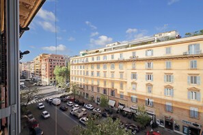 A multi-story building with a row of windows and balconies, a street with parked cars, and a clear blue sky. - 4bnb - Leone IV Apartment (Rome)
