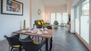 Un'area pranzo moderna con un tavolo di legno apparecchiato per due persone, un divano verde con cuscini gialli e un'ampia finestra vista esterna.