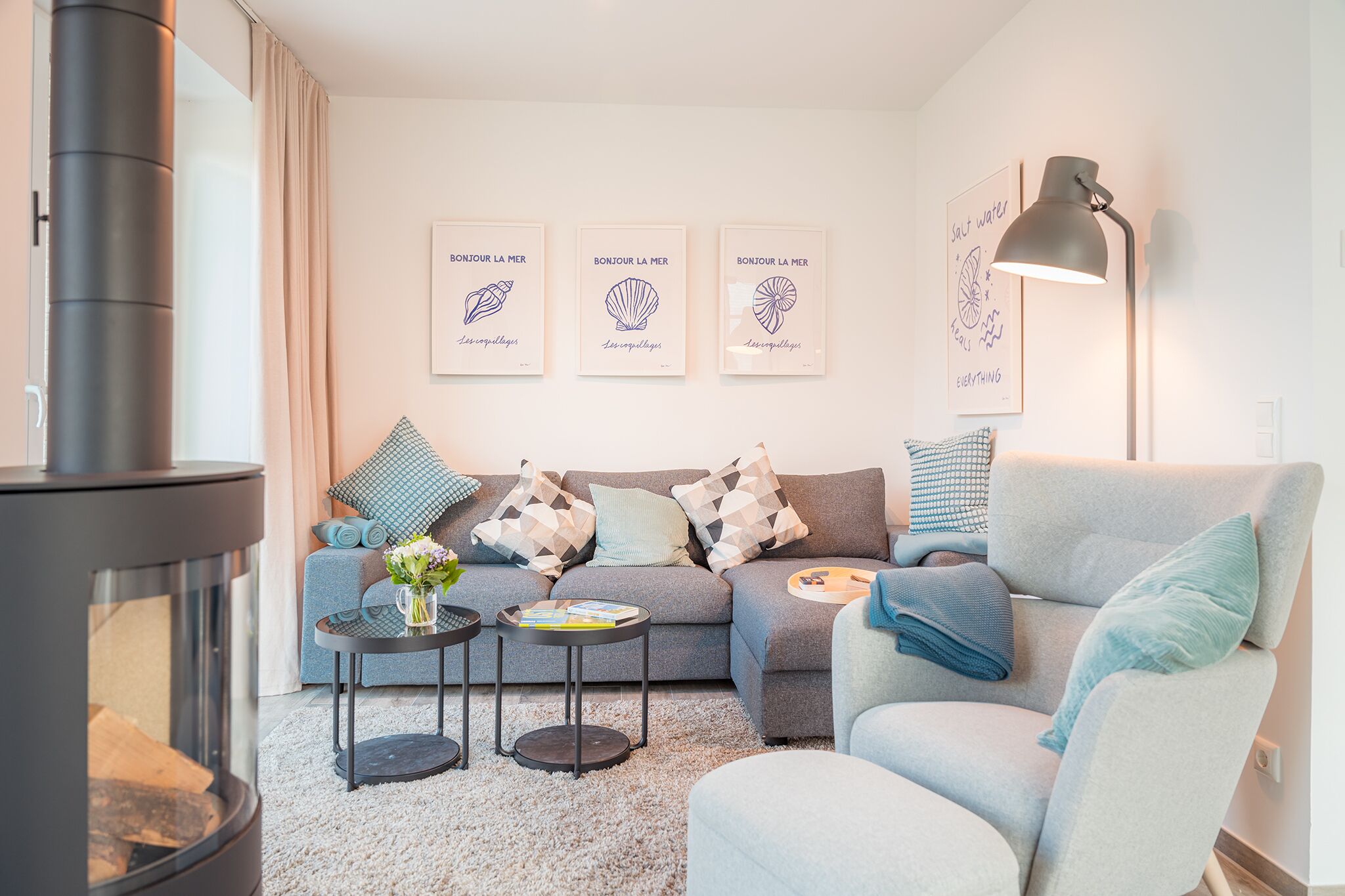 A modern living room with a sofa, coffee table, and fireplace. There are three framed artworks on the wall and a lamp on the right.