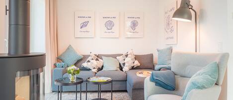A modern living room with a sofa, coffee table, and fireplace. There are three framed artworks on the wall and a lamp on the right.