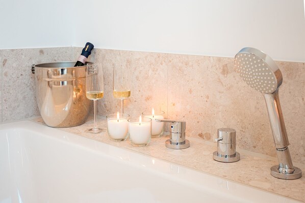 A bathroom with a bathtub, a champagne bucket, and three lit candles.