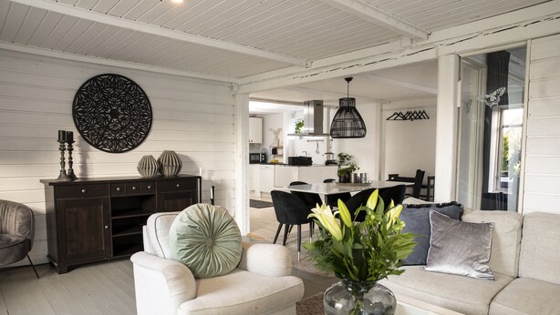 Een ruime woonkamer met een witte bank, een donker houten kast en een eethoek met tafel en stoelen.