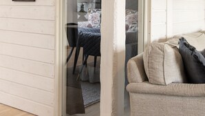 Een kamer met een schuifdeur die leidt naar een slaapkamer met een bed en een stoel. Er hangen afbeeldingen in lijsten aan de muur.