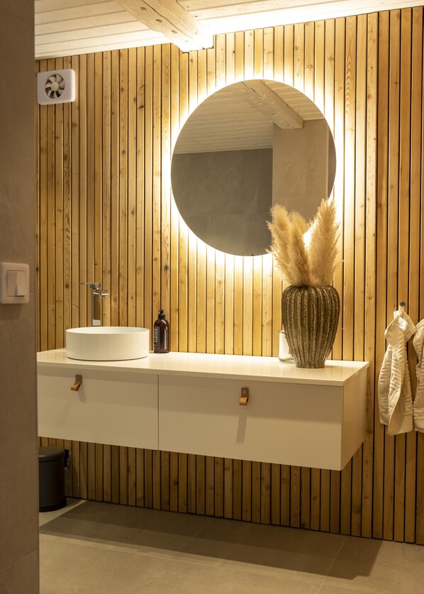 A bathroom with wooden paneling, a round mirror, a white sink, and a vase with pampas grass.