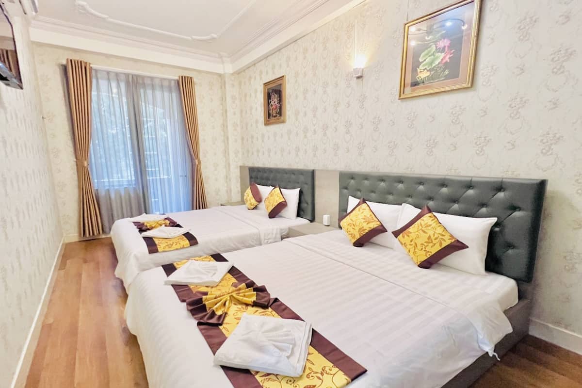 Ein Hotelzimmer mit zwei Betten, jeweils mit einem gesteppten Kopfteil, weißer Bettwäsche und Zierkissen. Das Zimmer verfügt über einen Holzboden, ein großes Fenster mit Vorhängen und ein gerahmtes Bild an der Wand.
