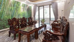 A spacious room with a large dining table surrounded by ornate chairs, a chandelier, and a mural of bamboo forest on the wall. - Truc Huyen Hotel (Ho Chi Minh City)