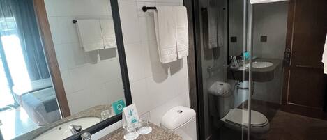 A modern bathroom with a large mirror, a granite countertop, a sink, a toilet, and a glass-enclosed shower.
