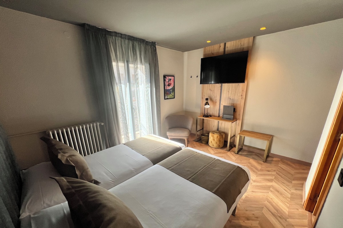 Quarto de hotel com uma cama grande, uma escrivaninha com computador, uma cadeira e televisão na parede.