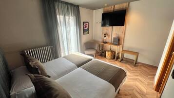 Habitación de hotel con una cama grande, un escritorio con computadora, una silla y un televisor montado en la pared.
