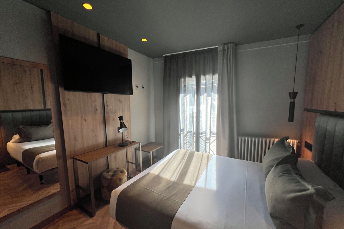 Una habitación de hotel moderna con una cama grande, un escritorio, una silla y un televisor montado en la pared.