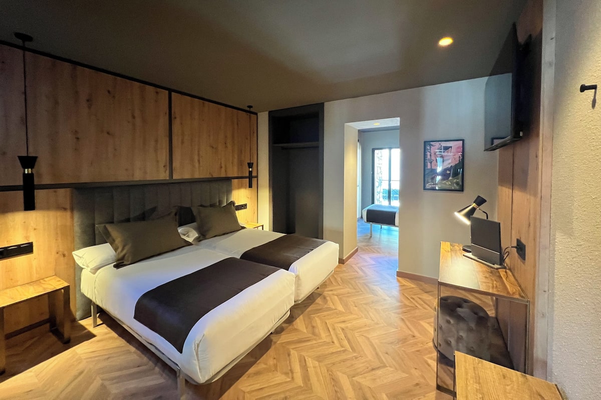 Um quarto moderno com uma cama grande, mesas de cabeceira e uma TV na parede.