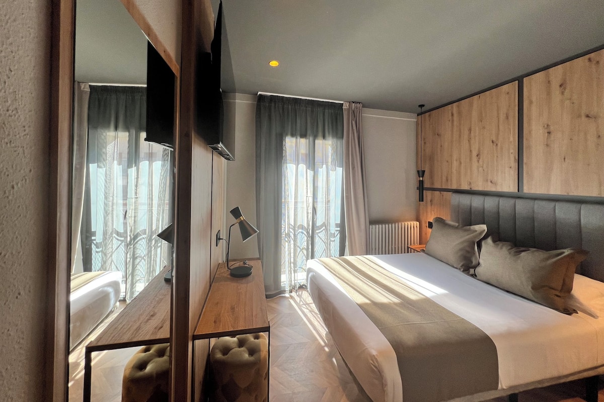 Quarto de hotel moderno com uma cama grande, uma escrivaninha de madeira, um espelho, uma televisão de tela plana e um radiador.