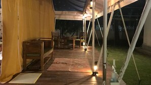 A tented outdoor area with wooden flooring, tables, chairs, and lanterns providing illumination. - Kumbh Village - Dining By Taj Ganges (Karchana)