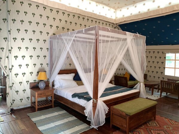 A four-poster canopy bed with a nightstand, a lamp, and a bench.