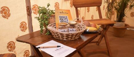 Una mesa de madera con un código QR, una cesta con frascos, una planta y una silla.