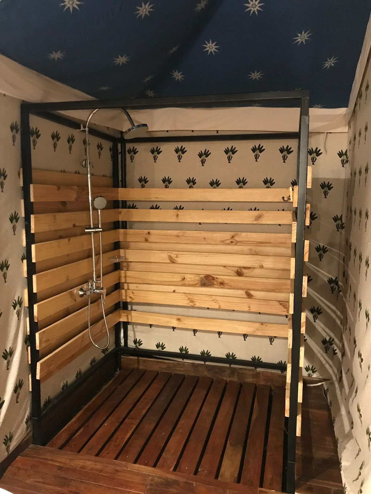 A small, enclosed wooden shower area with a metal frame and a showerhead.
