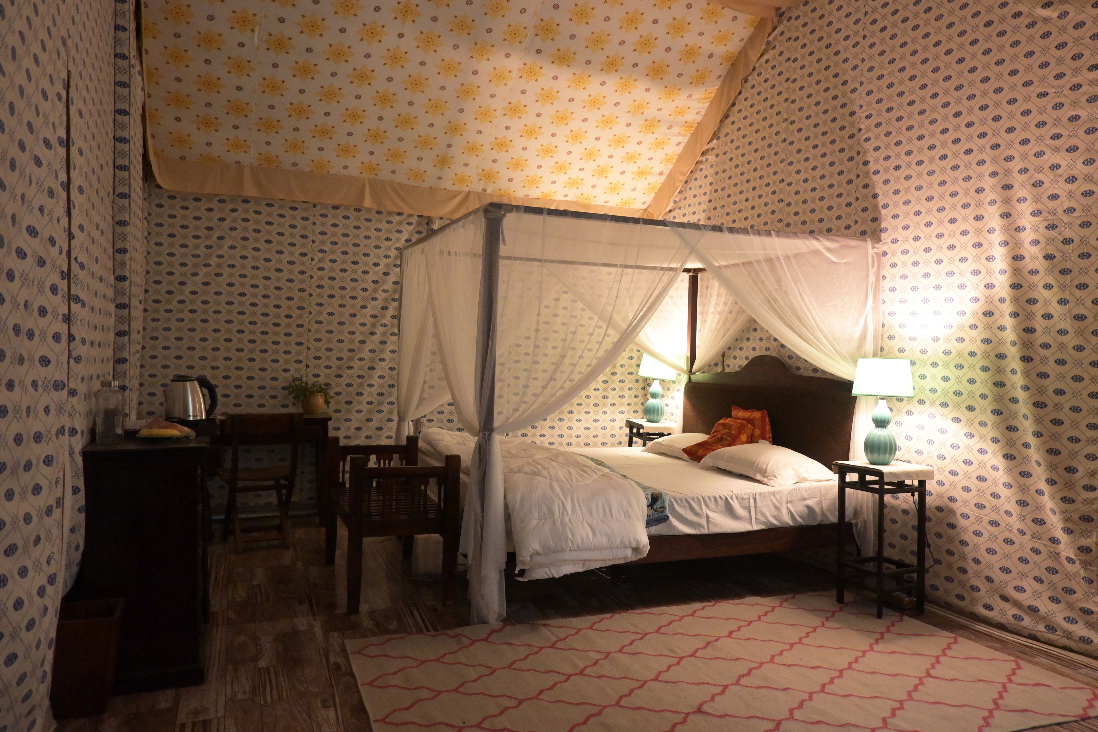 Un dormitorio con cama con dosel, una mesita de noche con lámpara y una silla.