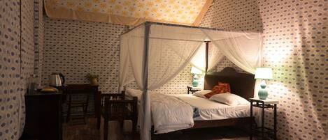 Un dormitorio con cama con dosel, una mesita de noche con lámpara y una silla.