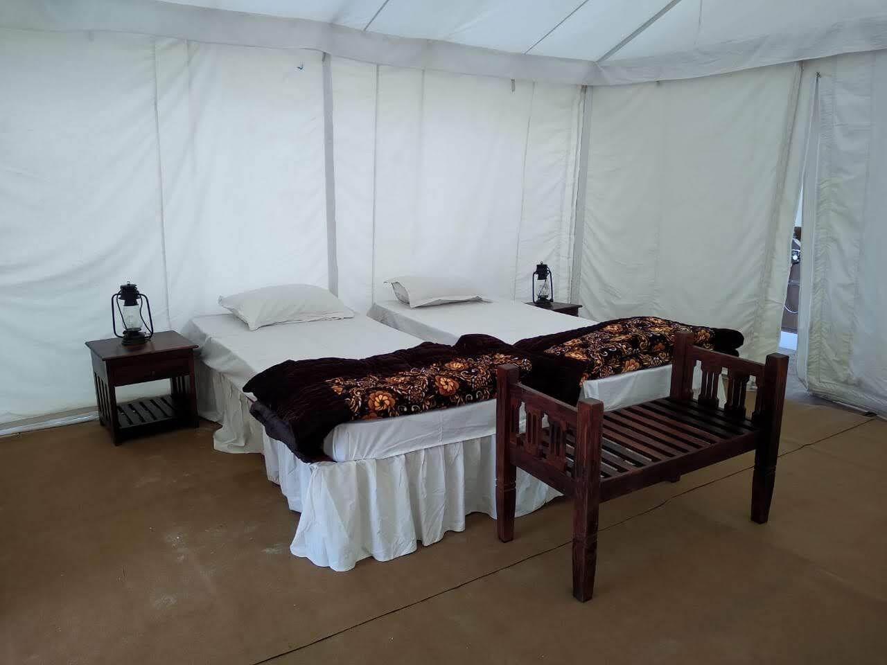 Une pièce aménagée avec une tente, comprenant deux lits, un banc en bois, une petite table avec une lampe et une lanterne.