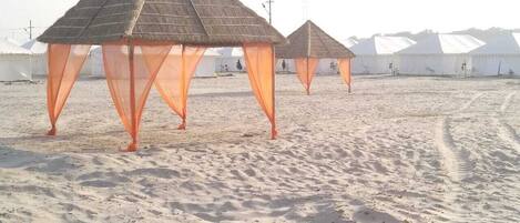 Una hilera de tiendas con techo de paja y cortinas anaranjadas en una playa de arena.