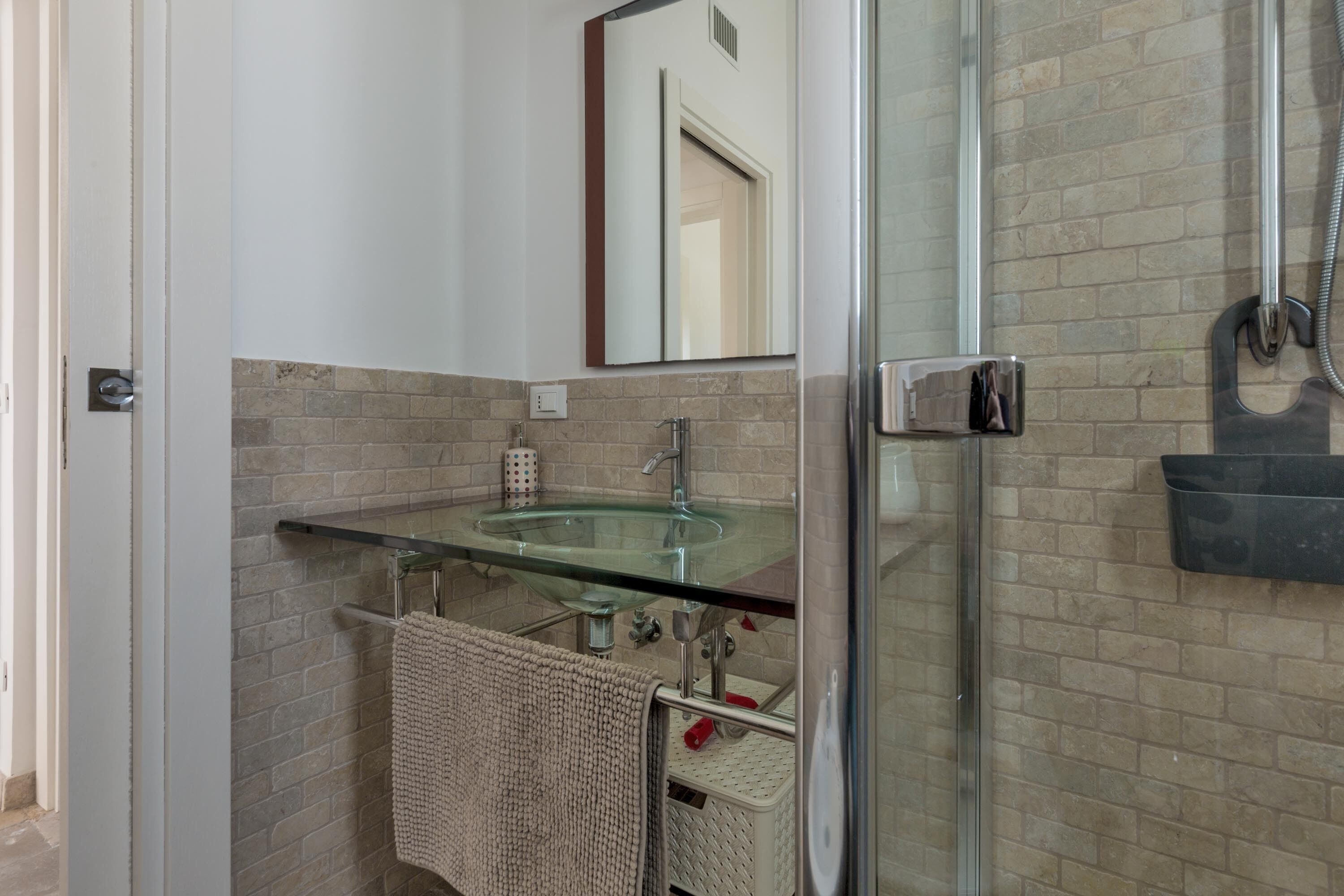 A bathroom with a glass sink, a towel rack, and a shower area.