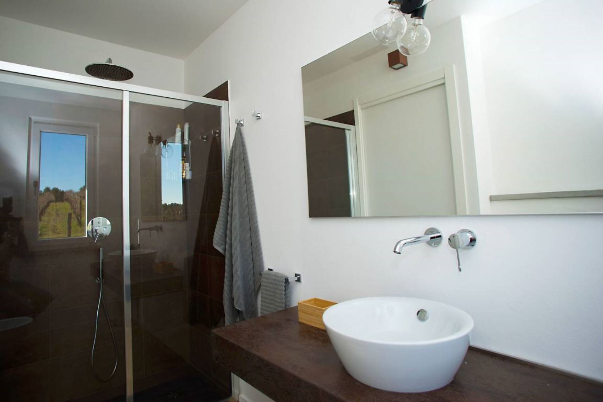 A modern bathroom with a glass shower enclosure, a large mirror, and a white sink on a dark countertop.