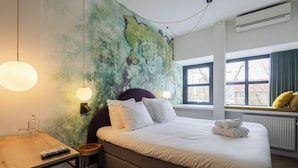 A hotel room with a bed, bedside table, lamp, and a view of the outside through a window. - Badhuis Hotel (Utrecht)