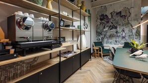 A modern kitchen with a coffee machine, shelves with decorative items, and a dining area with chairs and a table. - Badhuis Hotel (Utrecht)