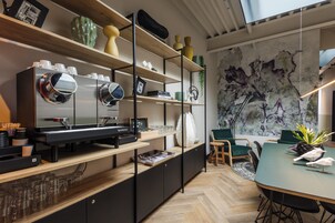 A modern kitchen with a coffee machine, shelves with decorative items, and a dining area with chairs and a table.