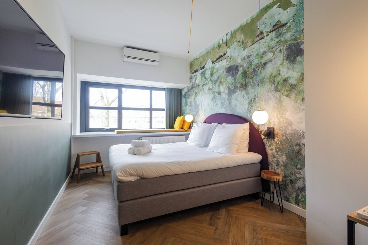A modern bedroom with a large bed, a window with a view, and a unique textured wall.