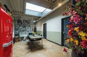 A modern office space with a large table, chairs, a red refrigerator, and a vibrant flower arrangement.