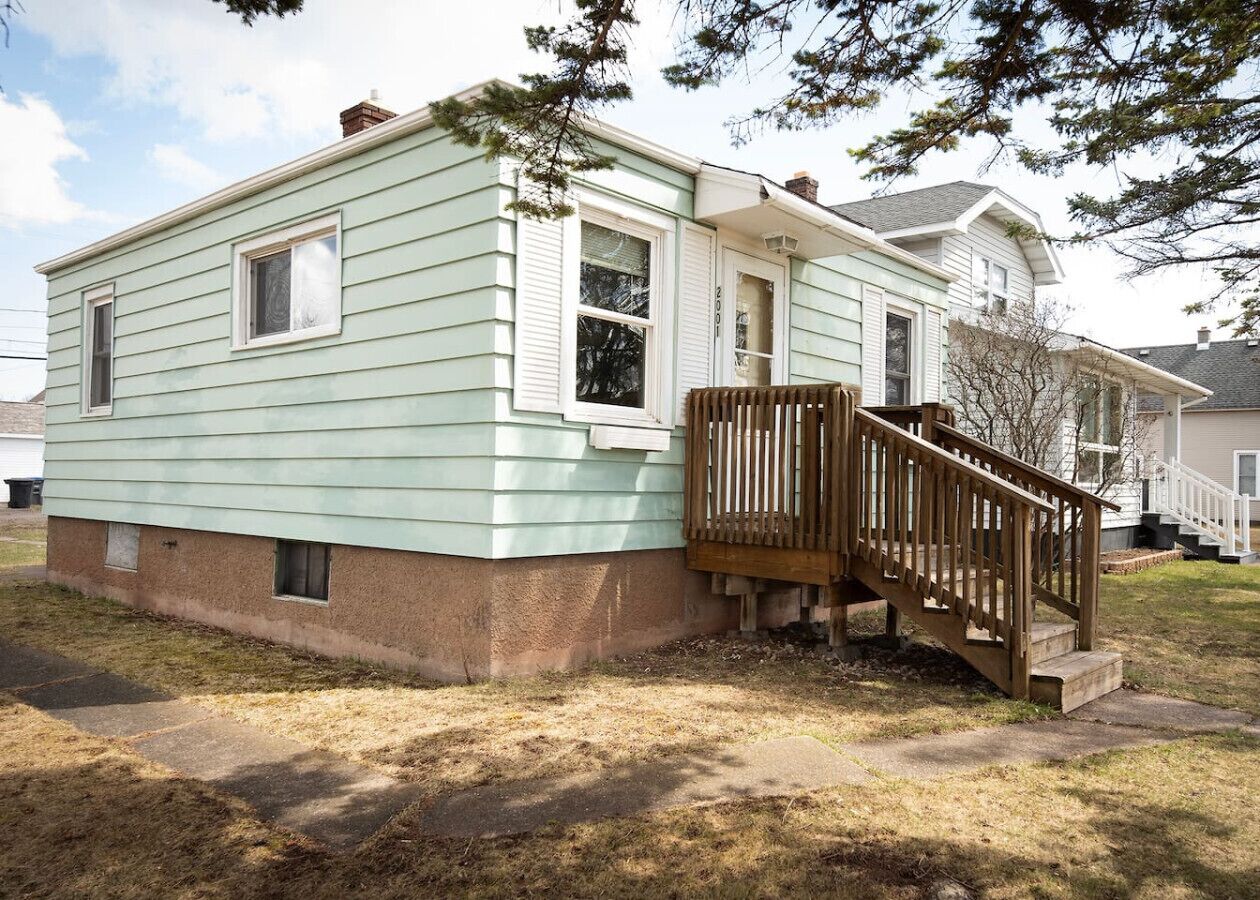 A single-story house with a front porch and a wooden staircase leading to the entrance.