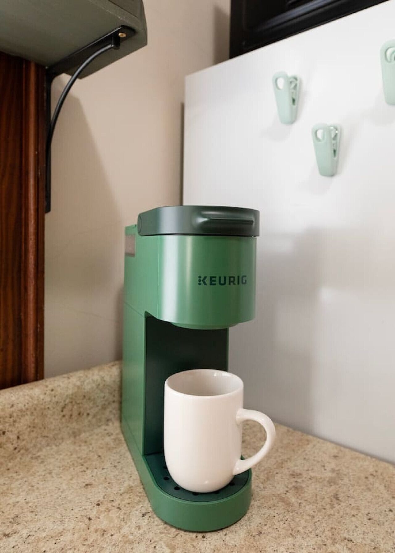 Eine Keurig-Kaffeemaschine mit einer weißen Tasse auf der Basis, platziert auf einer Küchenarbeitsplatte.