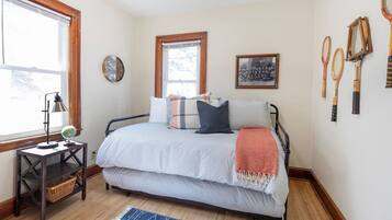 A bedroom with a bed, a nightstand, a window, a wall clock, and tennis rackets on the wall.