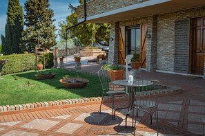 Un patio al aire libre con piso de ladrillo, una mesa redonda con sillas y plantas en macetas.