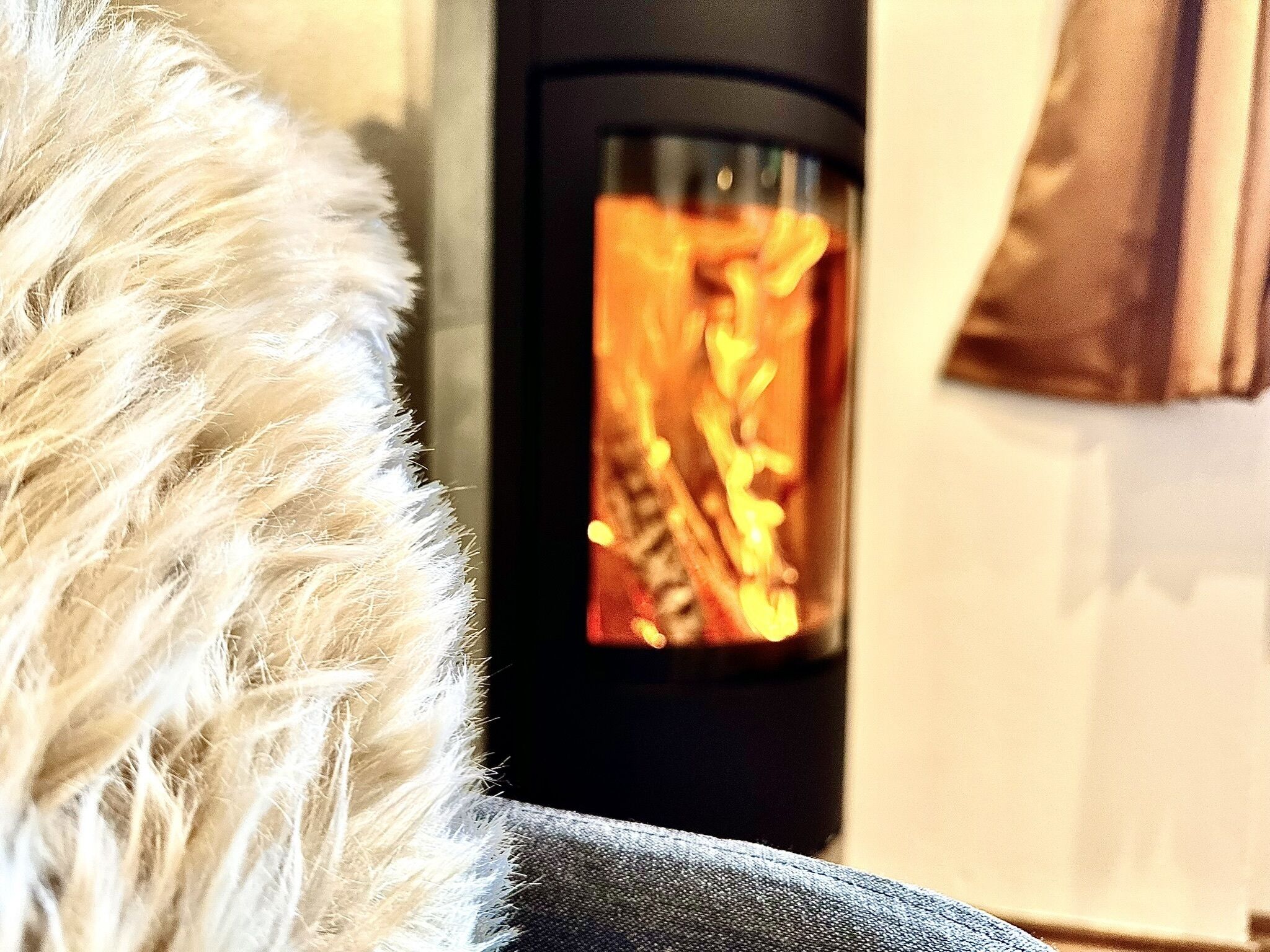 Eine Nahaufnahme eines fellüberzogenen Objekts, möglicherweise ein Sessel oder Sofa, mit Kamin im Hintergrund.