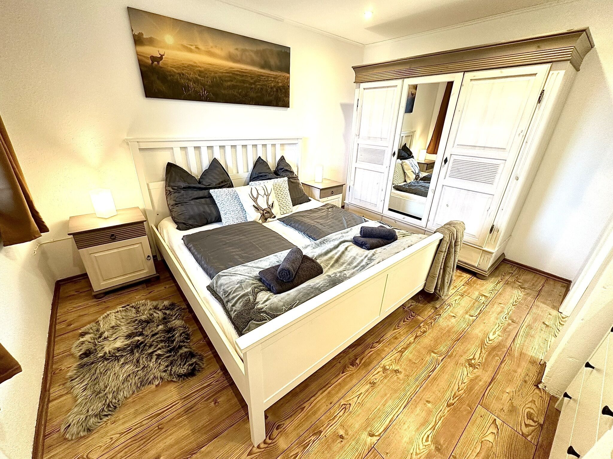 Ein Schlafzimmer mit einem Bett, einem Nachttisch, einem Fellteppich, einem Gemälde und einem Kleiderschrank.