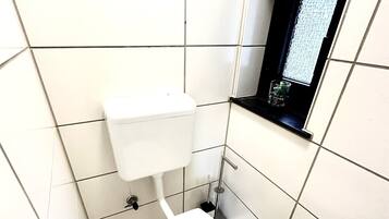 Pieni, moderni kylpyhuone, jossa on valkoiset laatat, wc-istuin, bidee ja ikkuna, josta on näkymä.