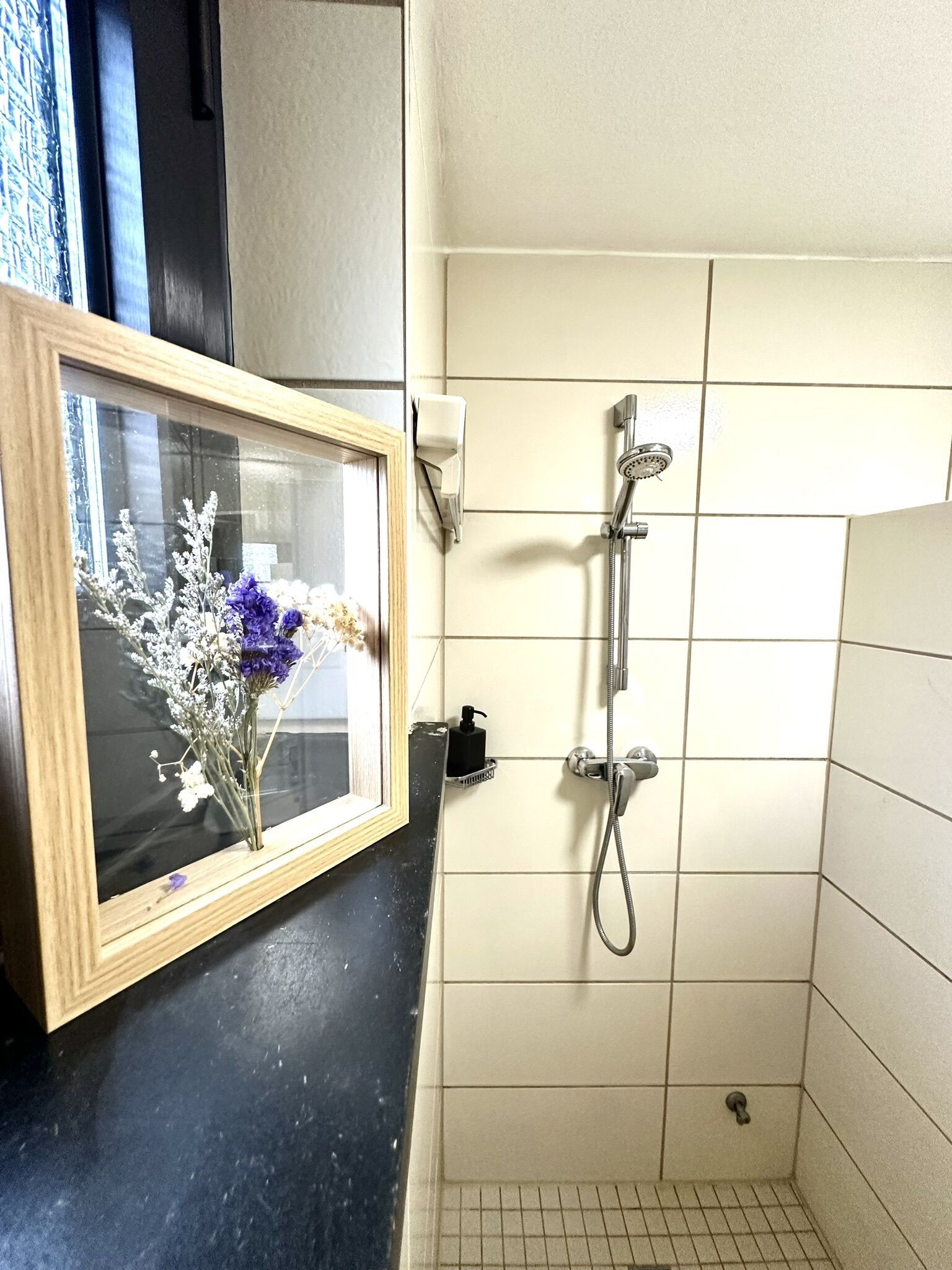 Un baño con ducha, un cuadro de flores y un dispensador de jabón.