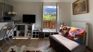 A cozy room with a bed, a desk with a computer, a TV, and a view of the outdoors.