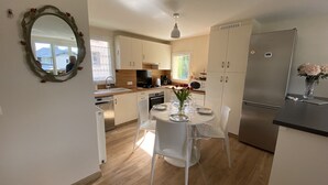 A modern kitchen with white cabinets, a stainless steel refrigerator, and a dining table set for four.