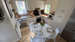 A compact kitchen with white cabinets, a microwave, a sink, and a dining table set for four.