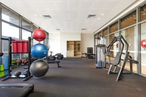Een sportschool met fitnessapparatuur, een loopband en een muur met ramen.