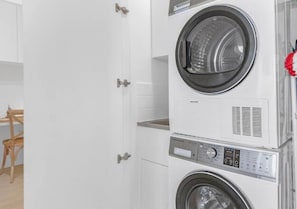 Een wasserette met gestapelde wasmachines en drogers, een houten stoel en een witte deur.