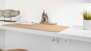 Un piano di lavoro bianco in cucina, con un tagliere, un contenitore metallico pieno di utensili e una pianta in vaso.