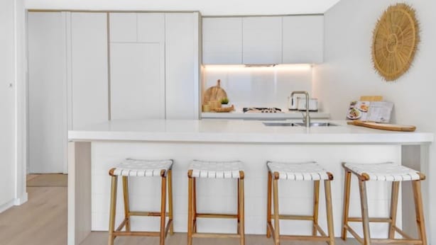 Una cucina moderna con mobili bianchi, un'isola centrale con sgabelli e una decorazione murale in fibre.