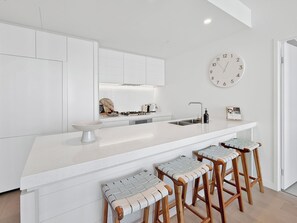 Une cuisine moderne avec des meubles blancs, un îlot central doté de tabourets, un évier et une horloge murale.